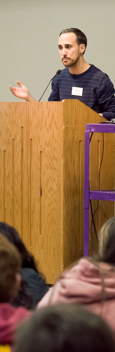 This photo shows Professor Annelli standing at a podium addressing a large group of visiting high school students and their teachers during a plenary session at the Language Festival in 2018.